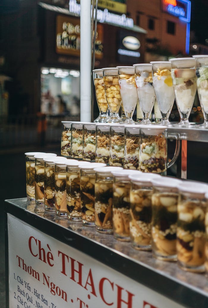 Street food stall featuring a variety of Vietnamese desserts in glass cups at night market.