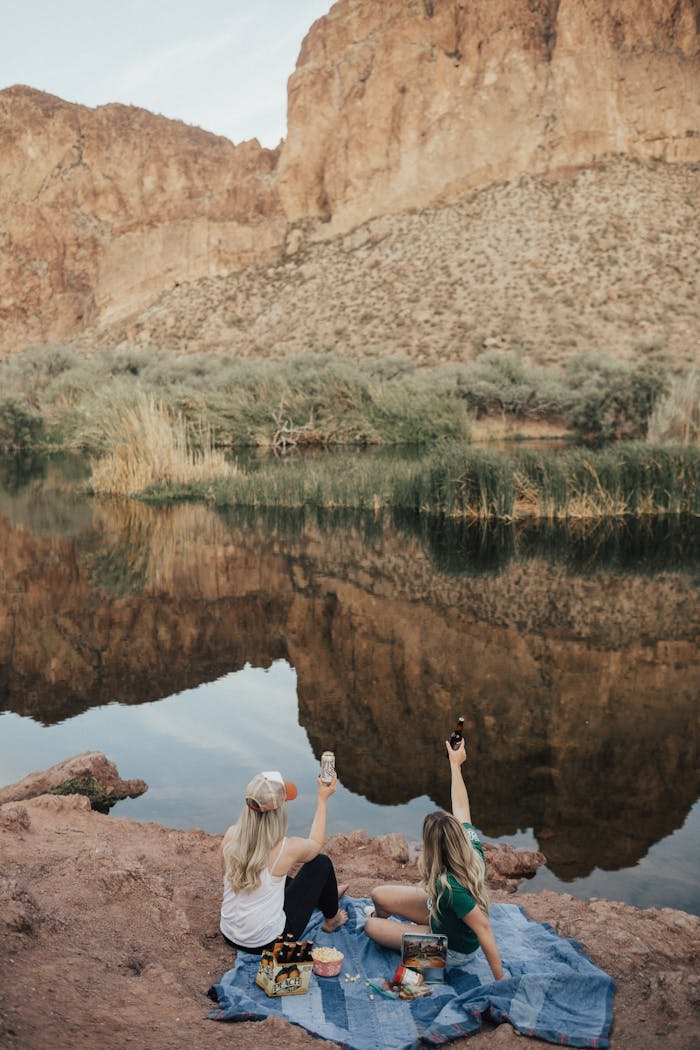 Two women enjoying a picnic by a serene lake with rocky canyon views.