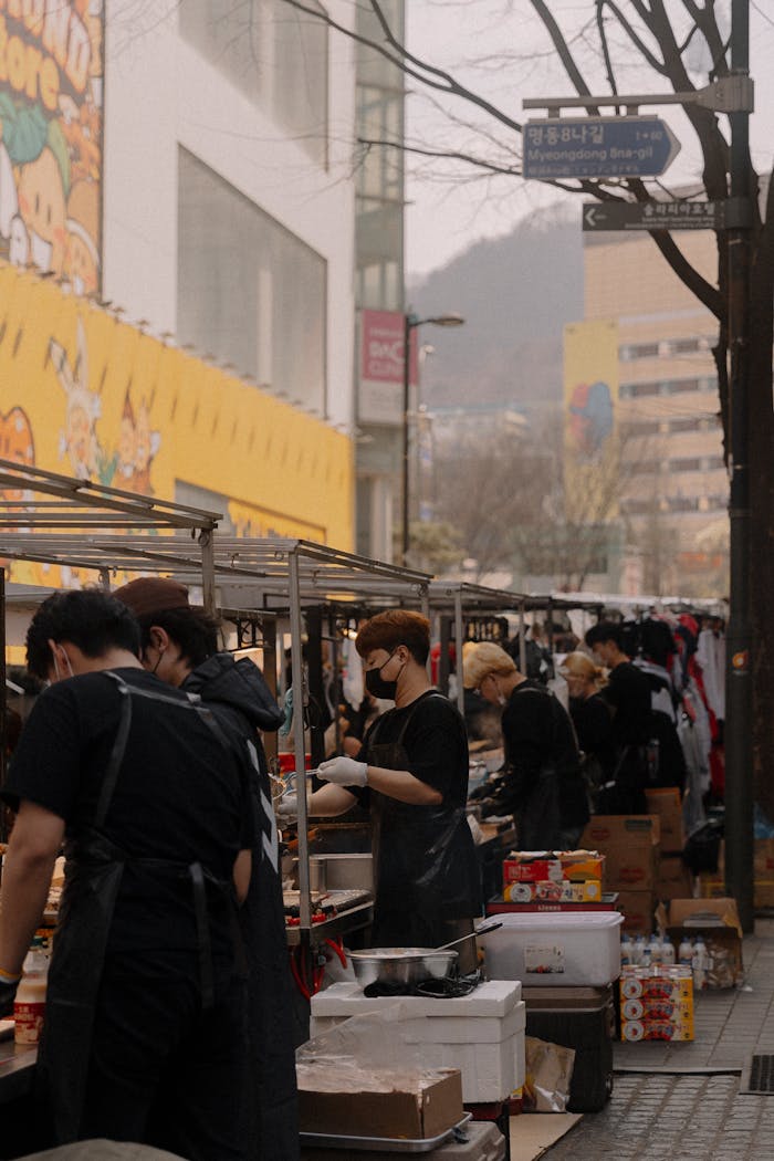 Urban street food market with vendors selling diverse cuisine in city setting.