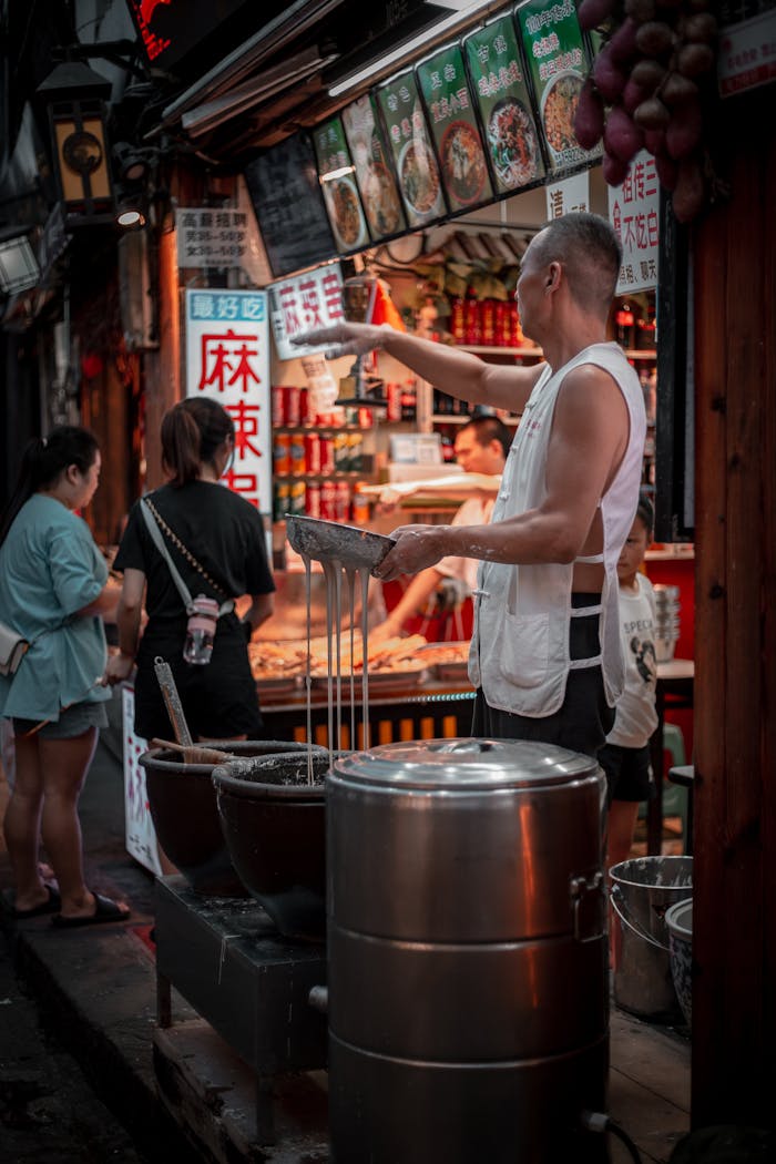 Street vendor in Chongqing, China, preparing traditional dishes in a bustling market setting.
