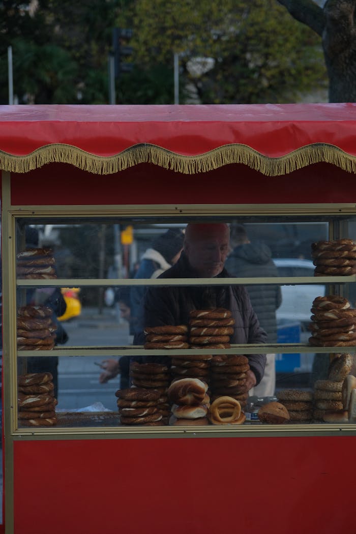 Man selling a variety of pretzels at a street stall with a red canopy, city background.